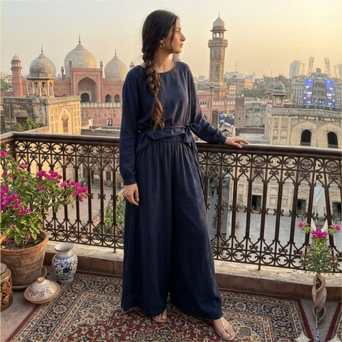 Woman in a blue dress standing on a balcony with a cityscape view, including historical buildings.