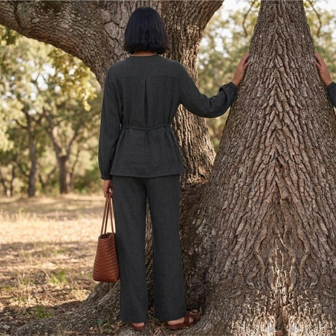 Person in a dark gray suit standing next to a large tree, holding a brown leather bag.