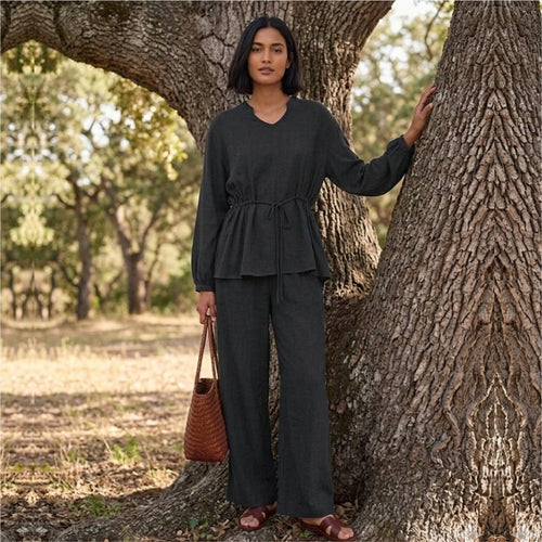 Woman in a dark outfit standing next to a tree in a natural setting